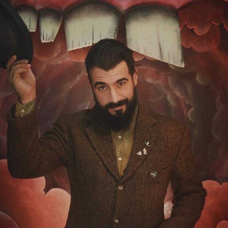 Le Turk, barbe et costume brun, soulève son chapeau au milieu d'une bouche géante en décor.